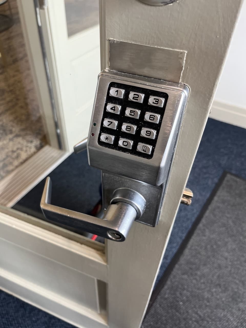 Silver electronic keypad door lock with a lever handle mounted on a light-colored door.