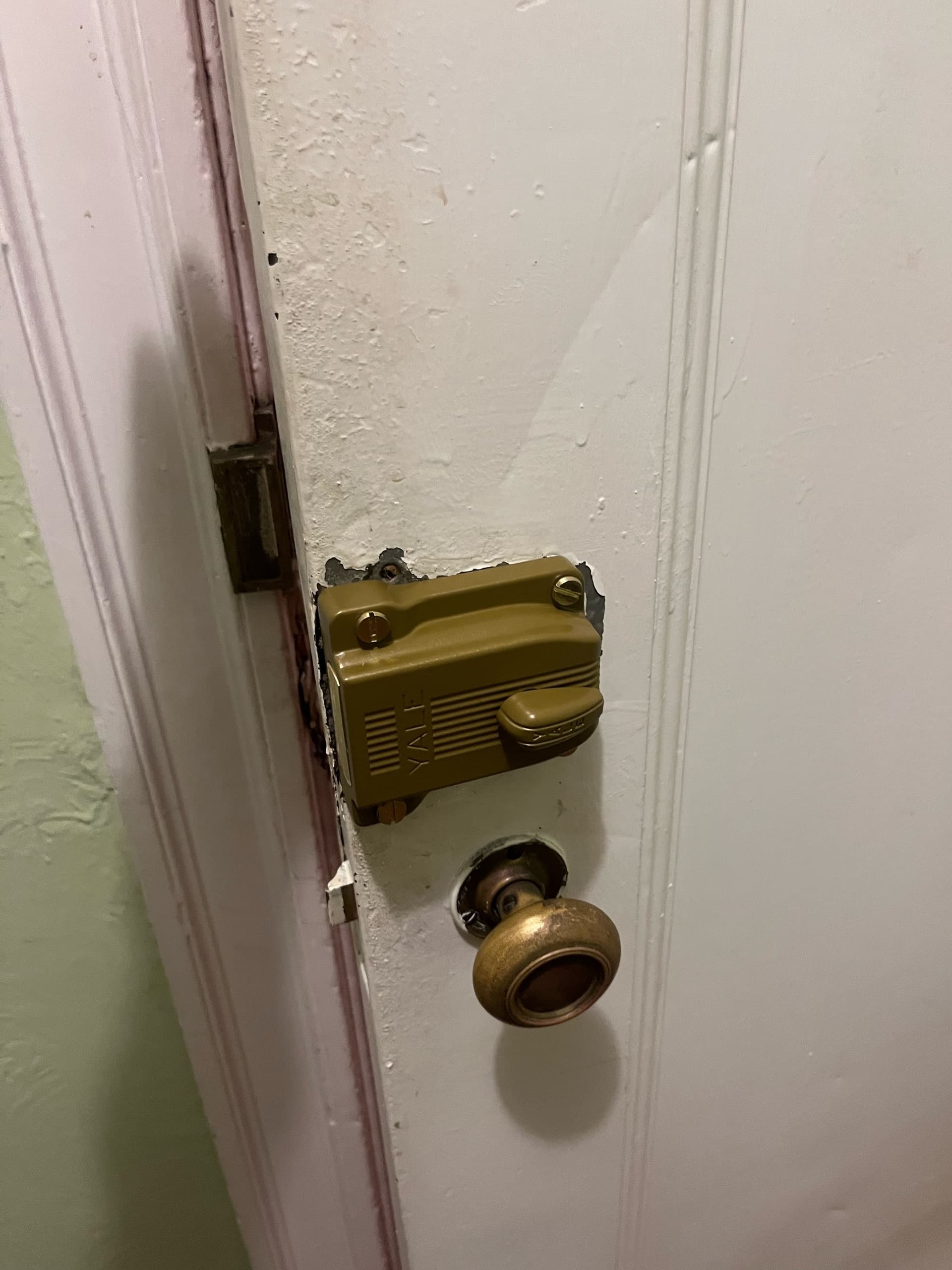 Vintage brass doorknob and brown Yale surface-mounted lock on a white painted wooden door.