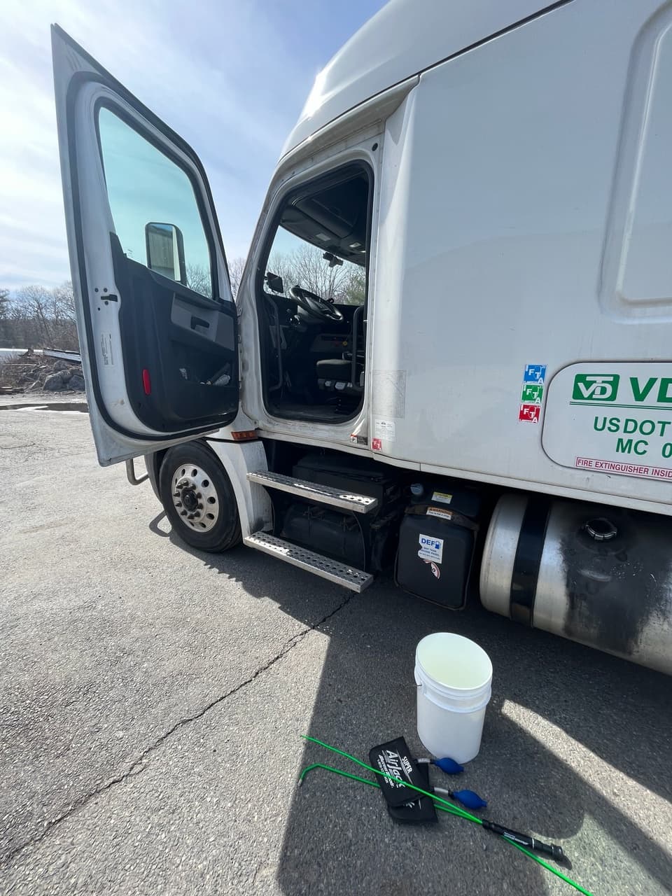 White semi-truck with driver's door open and lockout tools on the asphalt ground.