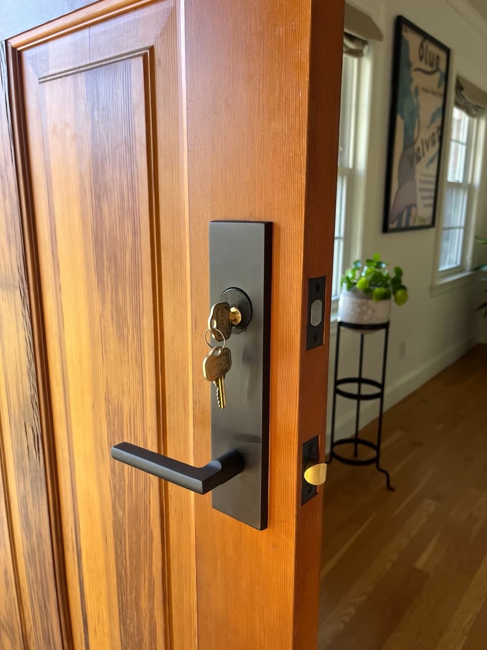 Black modern door handle and lock with keys inserted into a light wooden door.