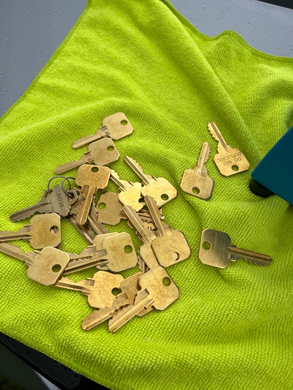 A pile of brass keys scattered across a bright lime green textured microfiber cloth.